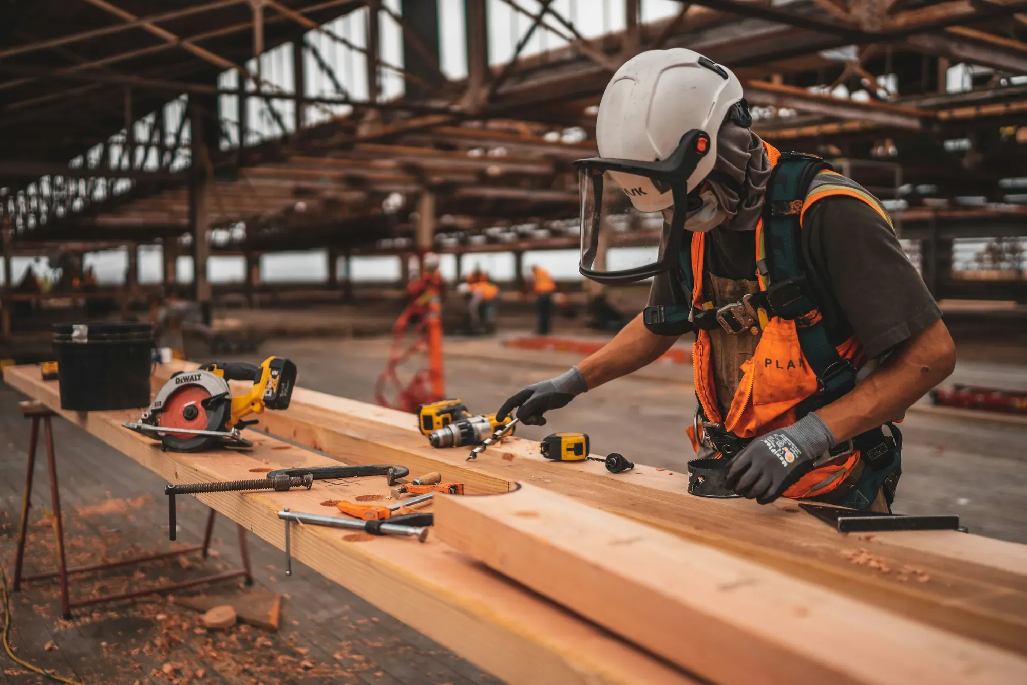 Construction worker in a hard hat and safety vest drilling into a wood beam